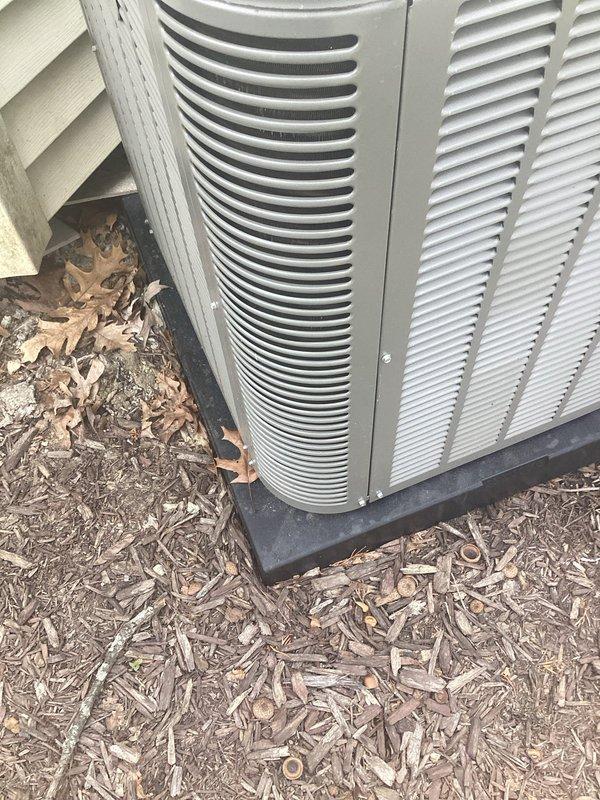 Responded to service call for outdoor air conditioning unit requiring releveling. Upon inspection, found condensing unit sitting unevenly on existing composite pad with inadequate support causing improper drainage from condensate pan. Unit positioned on wood mulch bed adjacent to building foundation with vinyl siding. Scheduled return visit to install proper leveling pads or S-cleats to correct equipment pitch and ensure proper condensate drainage. Unit currently operational but requires leveling correction to prevent future drainage issues and potential compressor strain from unlevel installation.