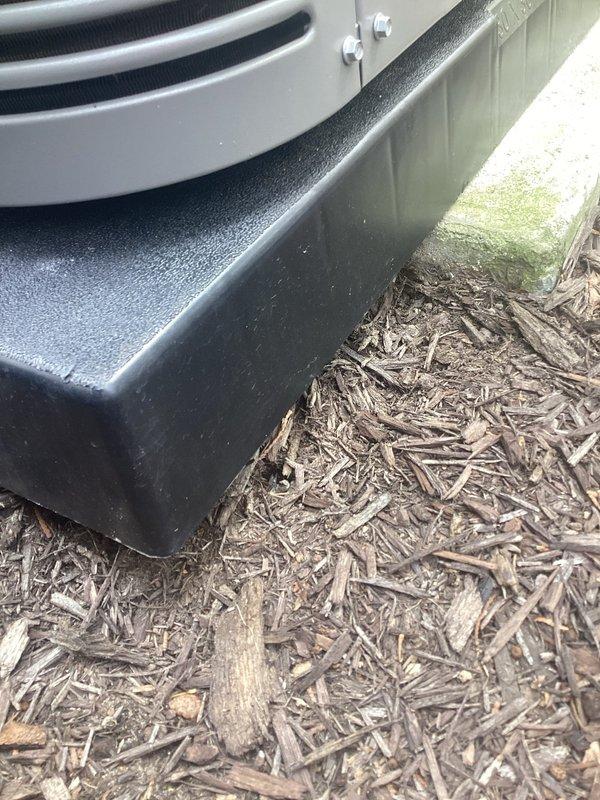 Responded to service call for outdoor air conditioning unit requiring releveling. Upon inspection, found condensing unit sitting unevenly on existing composite pad with inadequate support causing improper drainage from condensate pan. Unit positioned on wood mulch bed adjacent to building foundation with vinyl siding. Scheduled return visit to install proper leveling pads or S-cleats to correct equipment pitch and ensure proper condensate drainage. Unit currently operational but requires leveling correction to prevent future drainage issues and potential compressor strain from unlevel installation.