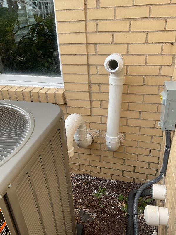 Completed full HVAC system installation including a 90,000 BTU furnace and 3.5-ton air conditioning unit with rear discharge configuration. Installed outdoor condenser unit on protective pad against exterior wall with refrigerant line set, electrical disconnect box, and white PVC condensate drain piping routed vertically along brick exterior. Reconnected all mechanical and electrical components, secured all piping and conduit, and verified proper system operation upon startup.
