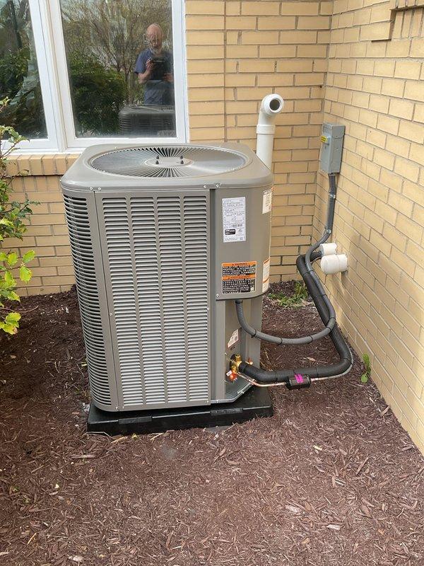 Completed full HVAC system installation including a 90,000 BTU furnace and 3.5-ton air conditioning unit with rear discharge configuration. Installed outdoor condenser unit on protective pad against exterior wall with refrigerant line set, electrical disconnect box, and white PVC condensate drain piping routed vertically along brick exterior. Reconnected all mechanical and electrical components, secured all piping and conduit, and verified proper system operation upon startup.