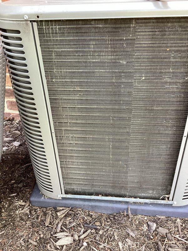 Performed annual cooling maintenance on residential split system. Inspected outdoor condenser unit and noted heavily soiled condenser coils with significant accumulation of dirt, dust, and debris restricting airflow. Continued refrigerant leak search investigation from previous summer service visit. Documented unit condition with photographs showing environmental contamination on heat exchanger fins and surrounding area. Assessed filter requirements for system optimization.