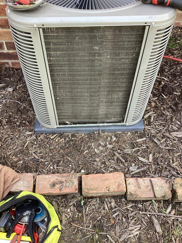 Performed annual cooling maintenance on residential split system. Inspected outdoor condenser unit and noted heavily soiled condenser coils with significant accumulation of dirt, dust, and debris restricting airflow. Continued refrigerant leak search investigation from previous summer service visit. Documented unit condition with photographs showing environmental contamination on heat exchanger fins and surrounding area. Assessed filter requirements for system optimization.