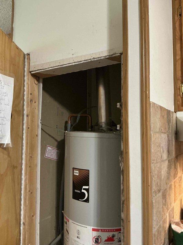Provided estimate for replacement of non-functional tanked water heater unit. Inspected existing Series 5 water heater installation in utility closet with exposed framing, noting vertical tank configuration with metal vent pipe extending through ceiling. Assessed plumbing connections, pressure relief valve, and venting requirements for standard tank-style water heater replacement to restore domestic hot water service.