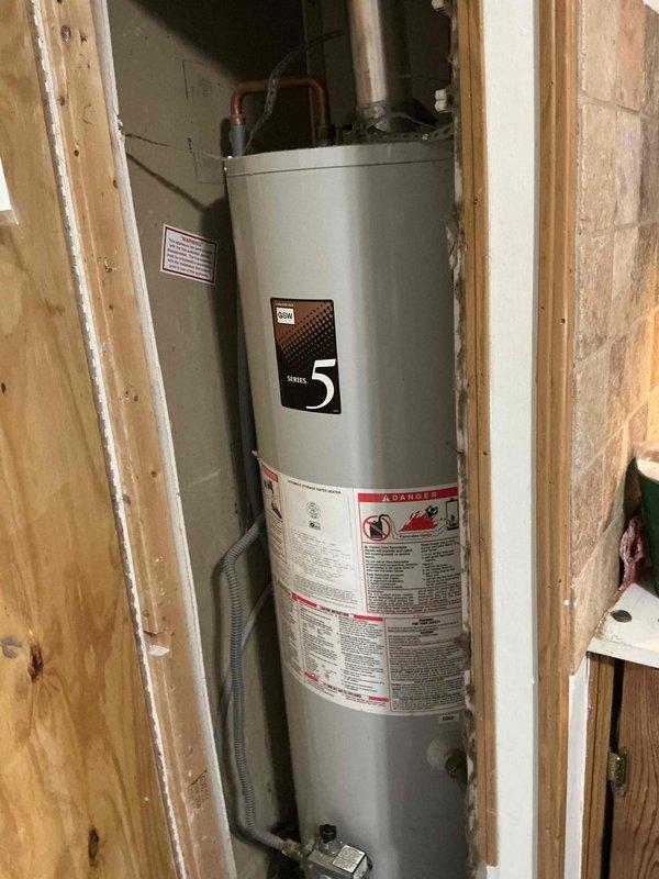 Provided estimate for replacement of non-functional tanked water heater unit. Inspected existing Series 5 water heater installation in utility closet with exposed framing, noting vertical tank configuration with metal vent pipe extending through ceiling. Assessed plumbing connections, pressure relief valve, and venting requirements for standard tank-style water heater replacement to restore domestic hot water service.