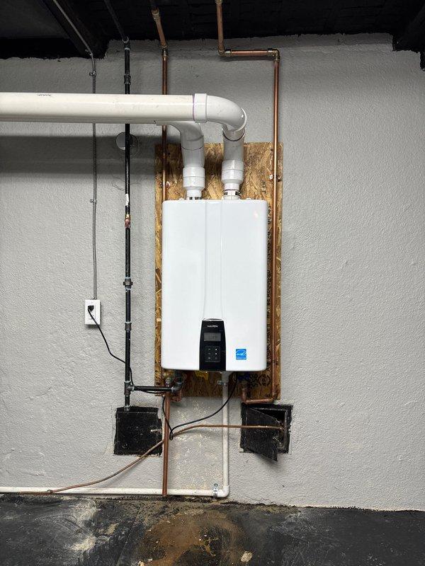 Completed installation of wall-mounted tankless water heater unit in basement utility area. Mounted unit on plywood backing board with proper structural support and installed new dedicated electrical circuit with conduit and outlet. Connected water supply lines using copper piping and installed white PVC venting system with proper elbows and horizontal runs to code specifications. Obtained and complied with mechanical and electrical permits for tankless water heater installation and new circuit work. Unit is Energy Star certified, fully operational, and venting properly through PVC exhaust system.
