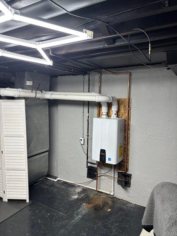 Completed installation of wall-mounted tankless water heater unit in basement utility area. Mounted unit on plywood backing board with proper structural support and installed new dedicated electrical circuit with conduit and outlet. Connected water supply lines using copper piping and installed white PVC venting system with proper elbows and horizontal runs to code specifications. Obtained and complied with mechanical and electrical permits for tankless water heater installation and new circuit work. Unit is Energy Star certified, fully operational, and venting properly through PVC exhaust system.