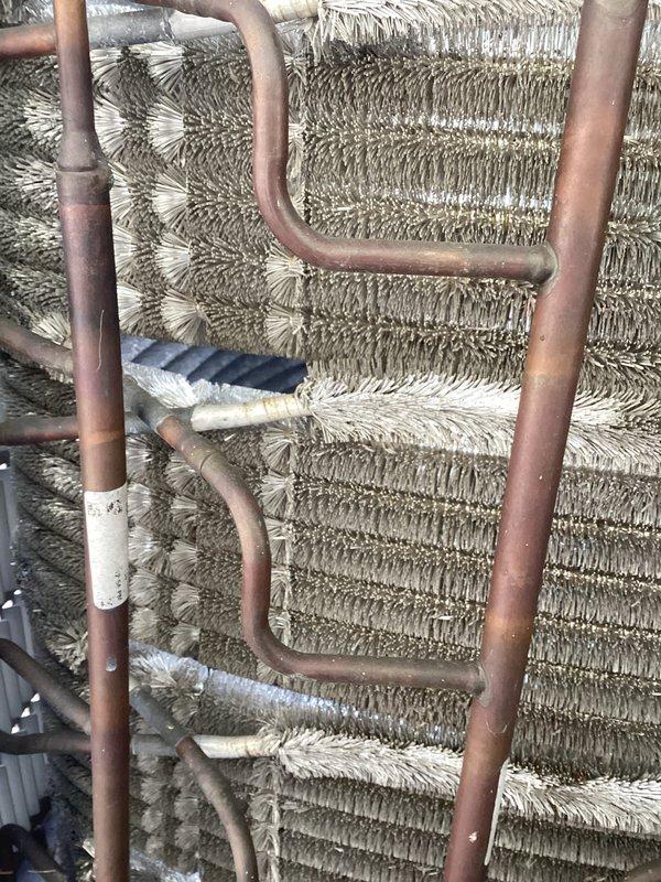 Completed preventive maintenance inspection on air handler unit. Performed visual examination of evaporator coil assembly, noting copper refrigerant lines and aluminum fin coils in operational condition. Documented heat exchanger components including parallel vertical copper tubing with U-shaped configurations and densely packed chevron-pattern aluminum fins. Verified refrigerant piping connections and couplings for integrity. Unit showing normal operational wear with surface oxidation on copper components consistent with age. All coil sections and mechanical components inspected and photographed for maintenance records.