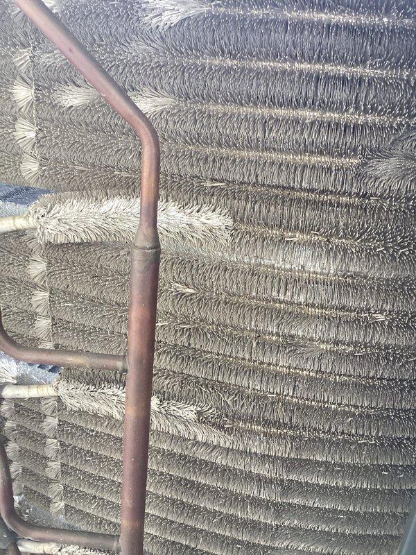 Completed preventive maintenance inspection on air handler unit. Performed visual examination of evaporator coil assembly, noting copper refrigerant lines and aluminum fin coils in operational condition. Documented heat exchanger components including parallel vertical copper tubing with U-shaped configurations and densely packed chevron-pattern aluminum fins. Verified refrigerant piping connections and couplings for integrity. Unit showing normal operational wear with surface oxidation on copper components consistent with age. All coil sections and mechanical components inspected and photographed for maintenance records.