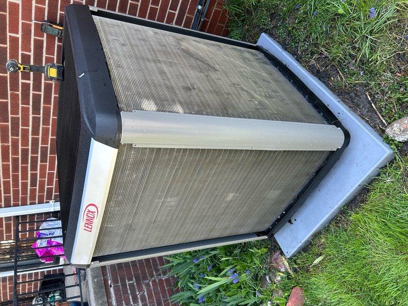 Completed annual preventative maintenance on outdoor condensing unit. Inspected V-shaped condenser coils which showed significant accumulation of dirt, dust, and debris on exterior surfaces and between fins. Documented unit condition with photographs showing heavy soiling on top panel and heat exchanger components. Unit operational at time of service with no immediate mechanical concerns noted, though coil cleaning recommended to maintain optimal heat transfer efficiency and system performance.