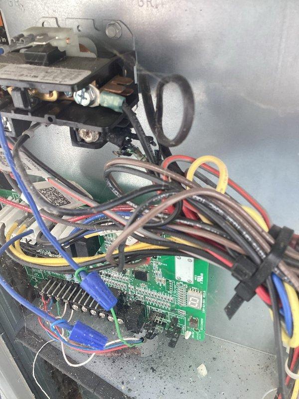 # HVAC Service Report - No Cooling Issue Resolved

Responded to service call for 2-year-old air conditioning system experiencing no cooling condition. Upon arrival, performed initial system diagnostics and visual inspection of outdoor condensing unit and indoor air handler components.

Accessed electrical control panel and thoroughly inspected all control boards, relay assemblies, and wiring connections. Examined black contactor relay with multiple copper terminal connections, verifying proper contact closure and electrical continuity. Tested all wire connections including blue, red, black, and yellow control and power wiring for secure termination and proper voltage readings.

Inspected multiple green printed circuit boards (PCBs) within the control housing, checking for signs of component failure, burned traces, or damaged electronic elements. Verified proper operation of all integrated circuits, capacitors, and resistors on control boards. Examined wiring harnesses and cable routing