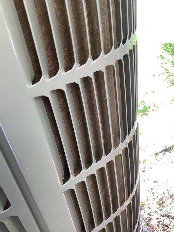 Responded to no cooling complaint on 7-year-old residential air conditioning system. Upon arrival, performed visual inspection of outdoor condensing unit. Examined exterior cabinet panels, louvers, and condenser coil fins for obstructions, debris accumulation, and airflow restrictions. Photographed unit condition showing louvered panels with minor dirt accumulation and condenser coil fins in relatively clean condition with proper spacing maintained. Verified unit accessibility and clearance from surrounding vegetation. Condenser coil fins displayed normal metallic appearance without significant blockage or damage. Cabinet structure intact with functional ventilation openings at top and bottom sections allowing proper airflow through heat exchanger assembly.