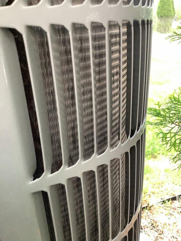 Responded to no cooling complaint on 7-year-old residential air conditioning system. Upon arrival, performed visual inspection of outdoor condensing unit. Examined exterior cabinet panels, louvers, and condenser coil fins for obstructions, debris accumulation, and airflow restrictions. Photographed unit condition showing louvered panels with minor dirt accumulation and condenser coil fins in relatively clean condition with proper spacing maintained. Verified unit accessibility and clearance from surrounding vegetation. Condenser coil fins displayed normal metallic appearance without significant blockage or damage. Cabinet structure intact with functional ventilation openings at top and bottom sections allowing proper airflow through heat exchanger assembly.