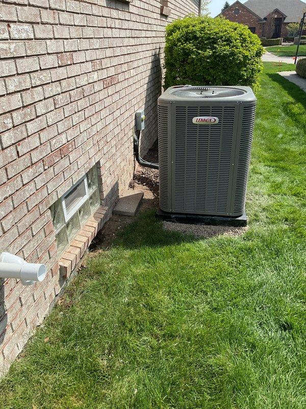 Completed return visit to finalize air conditioning installation. Retrieved Lennox condensing unit from garage and positioned it on prepared concrete pad adjacent to existing HVAC equipment on side of residence. Installed unit on level pad in accordance with manufacturer specifications, ensuring proper clearances from building structure and surrounding landscaping. Verified condensate drain line installation with white PVC piping extending from foundation area. Both Lennox condenser units now properly positioned on concrete pads with adequate spacing for airflow and serviceability. System placement allows for efficient operation and future maintenance access. Installation completed per customer's specific request for original technician return.