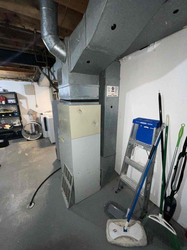 Provided estimate for complete HVAC system replacement in a mother-daughter home with a 30-year-old non-functional air conditioning unit and natural gas furnace located in the basement. Assessed existing vertical furnace/air handler with gray sheet metal ductwork and aged exterior condenser unit with cylindrical coil on concrete pad. Recommended full system replacement due to equipment age and current system failure.
