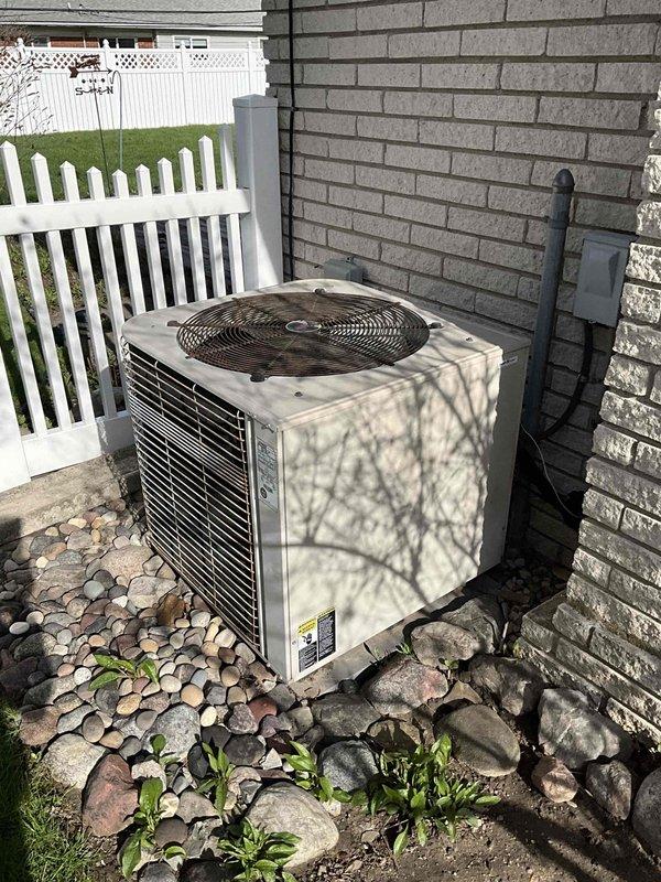 Provided estimate for complete HVAC system replacement including air conditioning condenser unit and furnace. Existing 24-year-old equipment is non-operational and has exceeded its serviceable lifespan. Documented current outdoor condenser unit positioned on decorative rock bed against exterior brick wall with electrical disconnect, and interior furnace installation in basement utility area with existing ductwork penetrations through insulated walls.