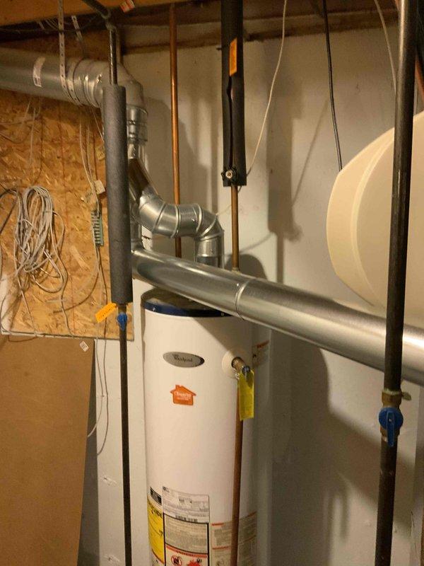 Responded to emergency call for leaking water heater requiring immediate replacement. Conducted on-site assessment of existing white cylindrical water heater installation in basement utility area. Documented current configuration including copper supply lines, black pipe connections with blue ball valve, existing electrical connections, and proximity to HVAC ductwork and electrical panel. Photographed equipment condition, plumbing connections, and surrounding mechanical systems to prepare comprehensive replacement estimate for failed water heater unit.