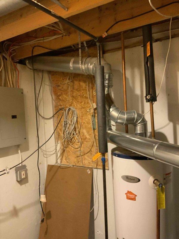 Responded to emergency call for leaking water heater requiring immediate replacement. Conducted on-site assessment of existing white cylindrical water heater installation in basement utility area. Documented current configuration including copper supply lines, black pipe connections with blue ball valve, existing electrical connections, and proximity to HVAC ductwork and electrical panel. Photographed equipment condition, plumbing connections, and surrounding mechanical systems to prepare comprehensive replacement estimate for failed water heater unit.