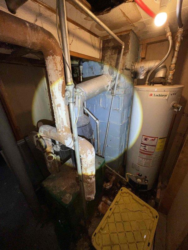 Provided estimate for complete HVAC system conversion from existing heating system to forced air in residential property. Assessed basement utility area containing aging water heater and deteriorating boiler unit with significant corrosion on piping, standing water on floor, and overall equipment wear indicating end of service life. Recommended full forced air system installation including new furnace, ductwork distribution throughout home, and proper drainage solutions to address moisture issues in mechanical room.