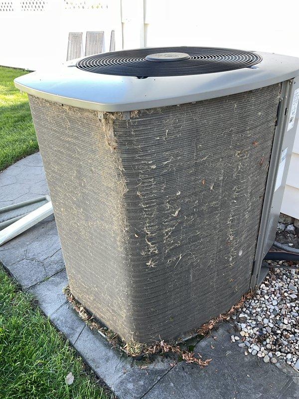 Completed annual cooling maintenance on residential air conditioning system. Inspected outdoor condenser unit, noting significant debris accumulation at base and deterioration of exterior fins requiring attention. Cleaned condenser coils, removed leaves and organic matter from unit perimeter, and verified proper operation of fan motor and compressor. Documented equipment condition with photos showing weathered fin material and environmental wear patterns on unit exterior.