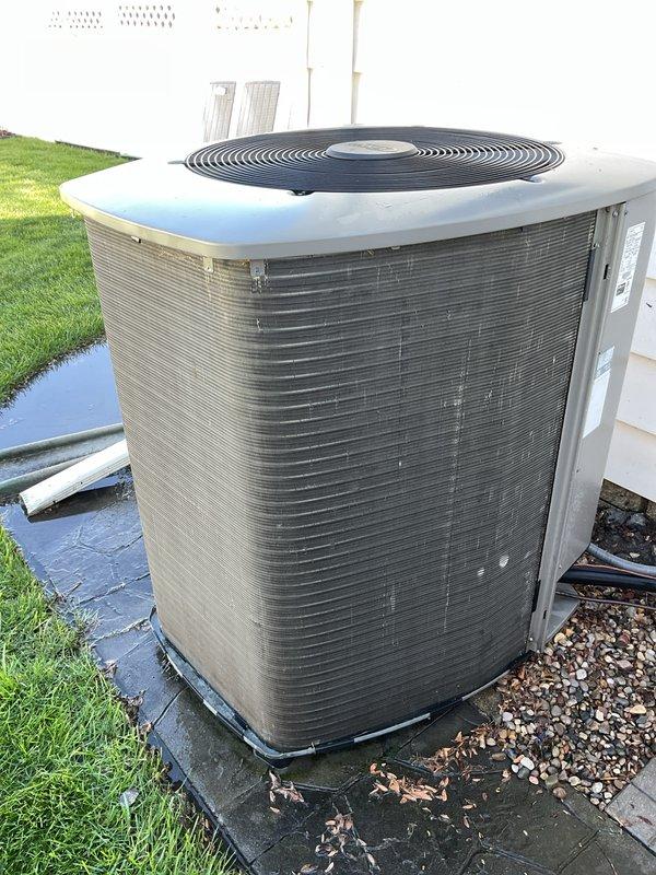 Completed annual cooling maintenance on residential air conditioning system. Inspected outdoor condenser unit, noting significant debris accumulation at base and deterioration of exterior fins requiring attention. Cleaned condenser coils, removed leaves and organic matter from unit perimeter, and verified proper operation of fan motor and compressor. Documented equipment condition with photos showing weathered fin material and environmental wear patterns on unit exterior.