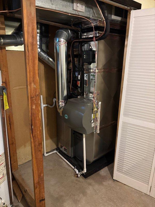 Completed full HVAC system installation including a 70,000 BTU furnace and 2-ton air conditioning unit with rear discharge configuration in residential basement utility area. Installed new furnace with proper venting through metallic flue pipe, connected white PVC condensate drainage lines at base, and ran copper refrigerant lines to outdoor condenser unit. Mounted equipment on concrete floor against wall with all ductwork properly sealed and connected to existing plenum system. Ran black electrical conduit and wiring through ceiling joists to power new equipment per code requirements. Installed whole-home humidifier integrated with furnace system. Reconnected all necessary utilities including gas, electrical, and drainage systems. Secured all necessary mechanical and electrical permits prior to installation. System tested and verified operational upon completion, with all components functioning within manufacturer specifications.