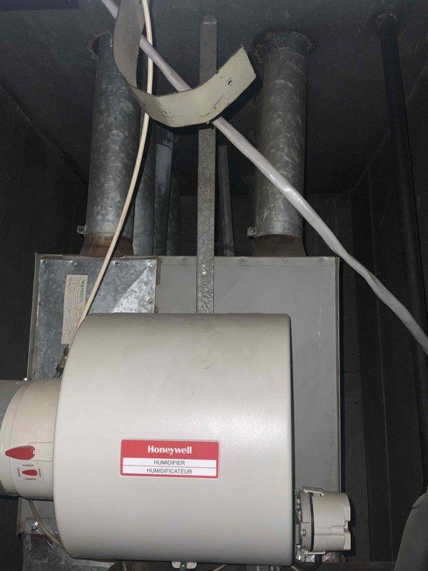 Provided estimate for replacement of 20+ year old furnace and air conditioning system located in living room closet on slab foundation. Current natural gas furnace operational but air conditioner not functioning. Existing system includes Honeywell humidifier unit with metal ductwork mounted in utility space showing typical wear and dust accumulation.