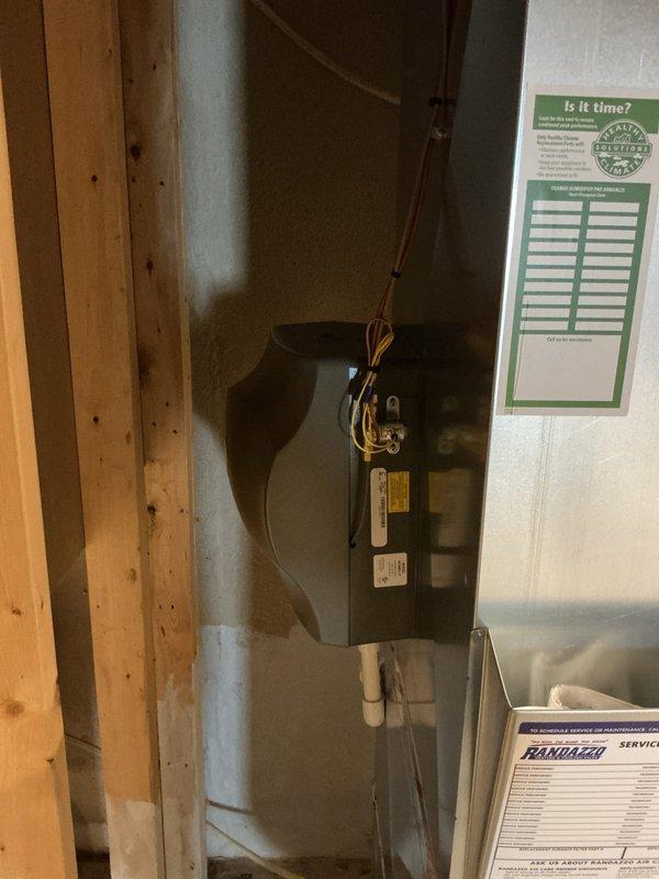 Completed full HVAC system installation including a 90,000 BTU furnace, 3.5 ton air conditioning unit, and humidifier. Air conditioning condenser unit positioned in left side yard with proper electrical and refrigerant line connections. Interior air handler installed in basement utility area with PVC condensate drain lines, all electrical connections completed, and system reconnected to existing ductwork. Mechanical and electrical permits obtained prior to installation, all equipment labeled and documented per code requirements.