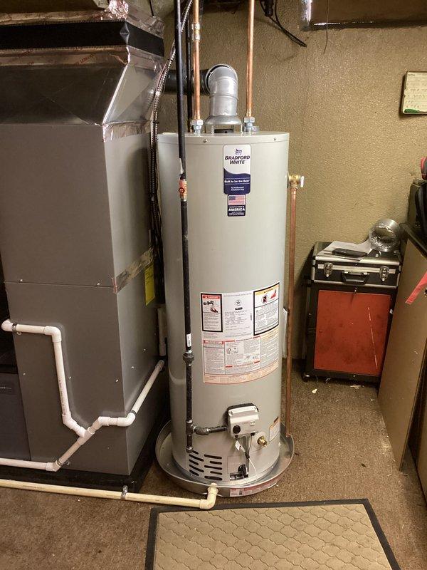Completed full HVAC system installation including a 70,000 BTU furnace with humidifier and liner, 2.5 ton air conditioning unit positioned on left side with exterior condensate drainage lines, and Bradford White water heater. All equipment installed in basement mechanical room with proper venting, copper supply lines, PVC condensate routing, and utility reconnections performed to manufacturer specifications.