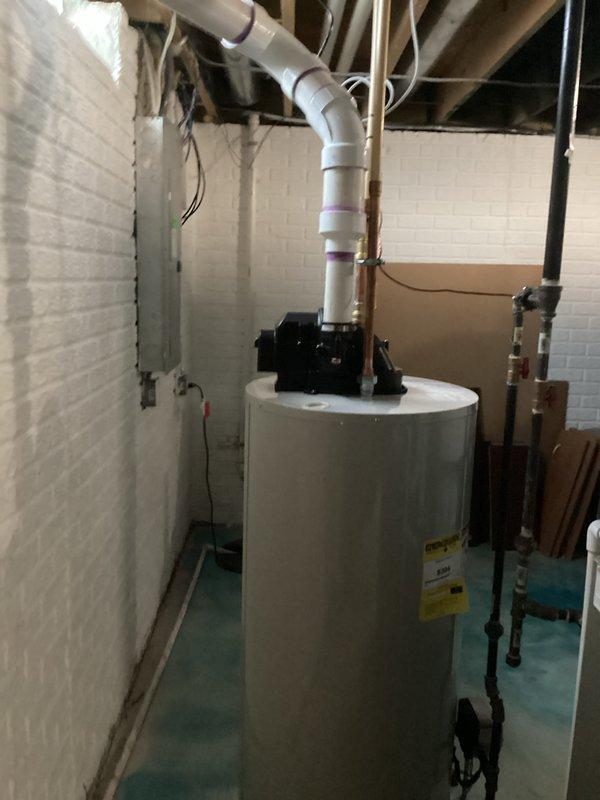 Successfully installed a 50-gallon tanked water heater in basement utility room. Removed existing unit and positioned new water heater on concrete floor, ensuring proper clearances and level placement. Connected hot and cold water supply lines using copper piping with appropriate shut-off valves and dielectric unions. Installed recirculation pump assembly on top of unit with associated black pump mechanism and PVC discharge piping routed vertically through ceiling joists. Made all necessary electrical connections to power the unit and pump system. Installed temperature and pressure relief valve with proper discharge piping termination. Tested all water connections for leaks, verified proper venting configuration, and ensured all plumbing code compliance requirements were met. Confirmed unit operational functionality including heating cycle, thermostat response, and recirculation pump operation. All manufacturer labels and specifications remain visible on front of tank for future refere