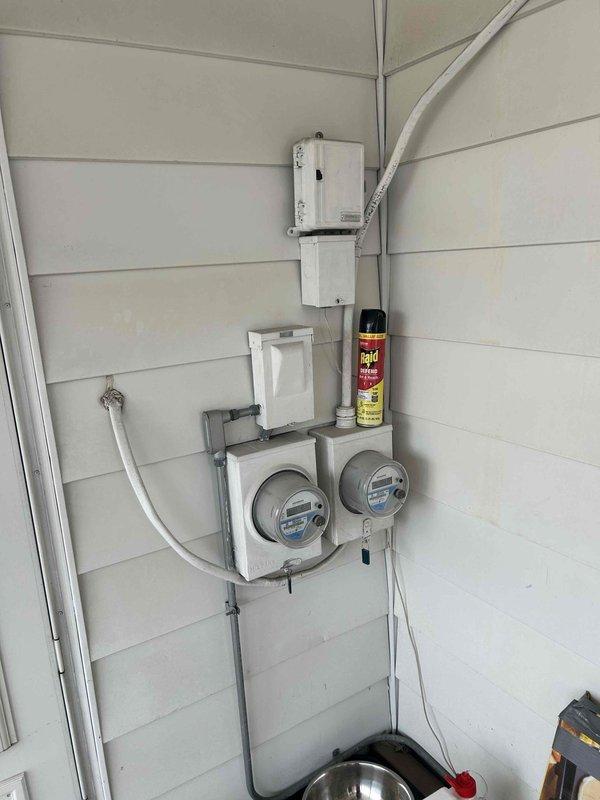 Performed on-site assessment for tankless water heater replacement at residential property. Evaluated existing tankless unit installation, including utility connections, gas metering configuration, and electrical service requirements. Documented current system setup with exterior utility infrastructure showing dual meter installation and electrical conduit routing. Inspected HVAC equipment area and utility access points to determine compatibility and clearance requirements for new tankless water heater installation.