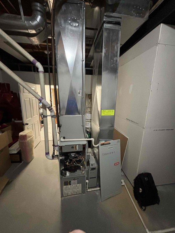 Conducted comprehensive assessment of 24-year-old non-operational natural gas furnace and air conditioning system located in lower level basement mechanical room. Evaluated existing gray metal furnace unit with exposed internal components, associated ductwork configuration, and outdoor condenser unit positioned on concrete pad with river rock landscaping against brick exterior wall. Provided detailed replacement estimate for complete HVAC system including furnace and air conditioning equipment to restore climate control functionality to residence.