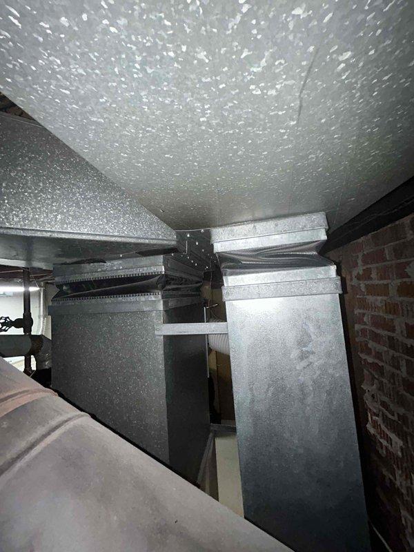 Conducted comprehensive assessment of existing HVAC system for full replacement estimate. Evaluated 20+ year old furnace and air conditioning equipment located in basement utility area, documenting current system configuration including ductwork distribution, venting arrangements, and equipment placement. Photographed existing furnace unit with black vent pipe installation and adjacent AC components to support replacement specifications and sizing requirements for new equipment installation.