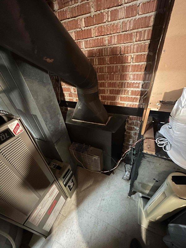 Conducted comprehensive assessment of existing HVAC system for full replacement estimate. Evaluated 20+ year old furnace and air conditioning equipment located in basement utility area, documenting current system configuration including ductwork distribution, venting arrangements, and equipment placement. Photographed existing furnace unit with black vent pipe installation and adjacent AC components to support replacement specifications and sizing requirements for new equipment installation.