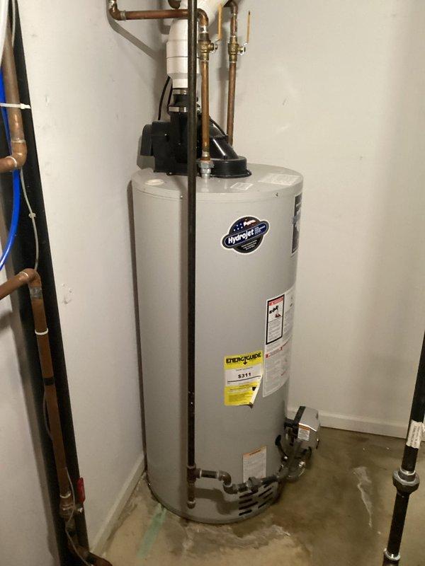 Responded to service call for leaking hot water tank in 31-year-old residential property. Upon inspection, identified active leak at base of Bradford White 50-gallon natural gas water heater (Model M-I-50US6N), which had reached end of serviceable life. Documented unit specifications, plumbing connections including copper supply lines with recirculation pump, gas shutoff valve, and visible water damage on concrete floor surrounding tank base, confirming immediate replacement required to prevent further water damage and restore hot water service.