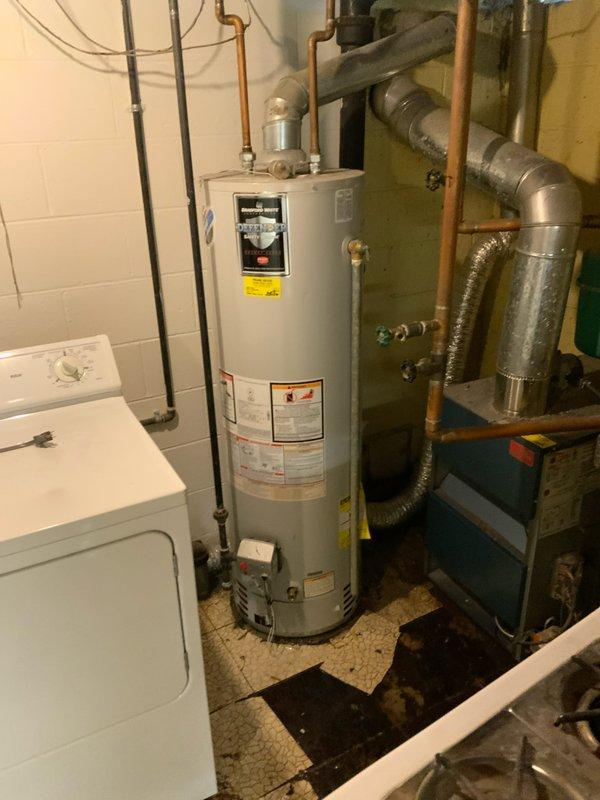 Provided estimate for replacement of non-functioning standard tank water heater in basement utility room. Assessed existing white cylindrical water heater with copper pipe connections, gas control valve, and supply lines requiring replacement. Customer requires consultation with contractor's authority due to boiler system integration considerations before proceeding with installation.