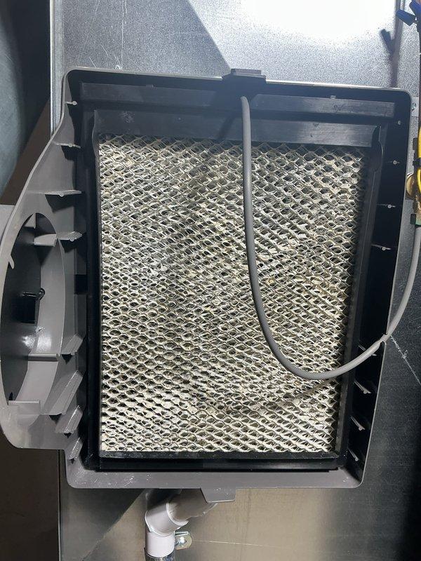 Completed scheduled air conditioning maintenance service on Lennox system. Inspected evaporator coil assembly which showed significant dust and debris accumulation on the honeycomb mesh surface, requiring attention. Replaced dirty air filter and evaporator pads per maintenance protocol. Verified thermostat operation displaying 66°F indoor temperature with system set to heat mode at 64°F target and 52% humidity level. System operational upon completion of maintenance tasks.