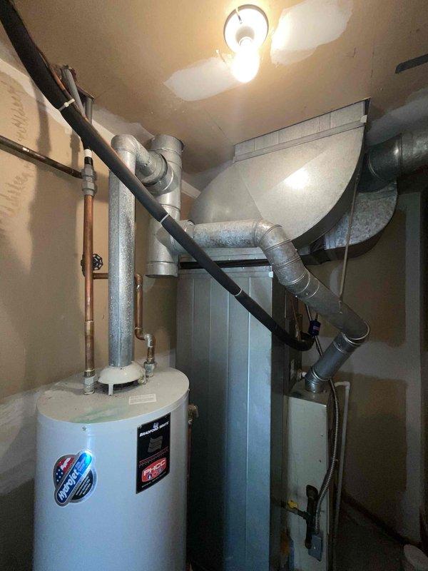 Provided estimate for replacement of existing standard tank-type water heater located in furnace room mechanical space. Current unit is operational but experiencing active leak, requiring replacement to prevent water damage and restore system integrity. Assessed installation area with existing copper supply lines, shut-off valves, and pressure relief valve configuration alongside HVAC ductwork and ventilation components in confined utility space.