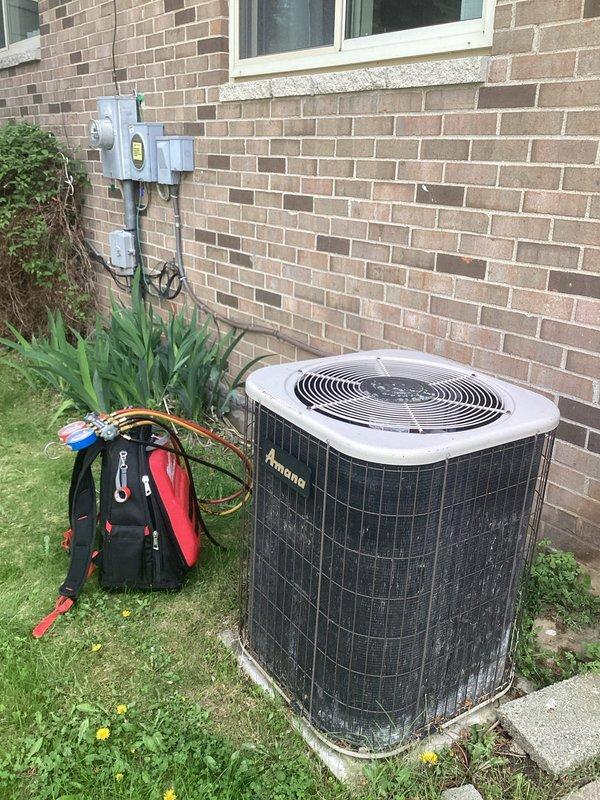 # HVAC Service Call - Air Conditioning System

Responded to service call for outdoor Amana air conditioning unit not cooling. Upon arrival, located condensing unit on concrete pad against exterior brick wall. Connected manifold gauge set to service ports to assess system pressures and diagnose cooling failure.

Performed visual inspection of condensing unit exterior condition, checking for obvious signs of damage, debris blockage in coil fins, or electrical issues at disconnect. Verified power supply at adjacent electrical meter and disconnect box. Evaluated compressor operation and fan motor function during diagnostic testing.

Measured refrigerant pressures on both high and low side of system using calibrated HVAC gauges to determine if system had adequate refrigerant charge or potential leak. Assessed temperature differential and system performance indicators to identify root cause of cooling deficiency. Equipment age noted as older with unknown service history, requiring thorough e