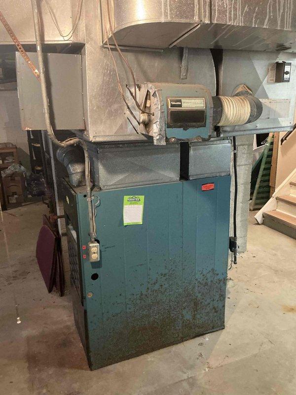 Conducted on-site assessment of approximately 40-year-old furnace system located in basement mechanical room for complete system replacement estimate. Evaluated existing heating equipment showing significant age-related wear, dust accumulation, and cabinet discoloration, with no current air conditioning system installed in the residence. Documented existing furnace configuration, blower assembly, motor housing, plenum connections, and electrical service panel with numbered circuit breakers. Inspected utility room infrastructure including concrete block walls, electrical conduit routing, and ductwork connections to determine installation requirements for new furnace and first-time central air conditioning system. Photographed existing equipment and electrical panel to support estimate preparation for full HVAC system replacement including both heating and cooling components.