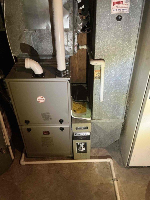 Responded to no cooling complaint for residential property with over 20-year-old air conditioning system that was non-functional. Completed full HVAC system assessment revealing existing Payne furnace in serviceable condition with Electro-air air handler present in basement utility area. Installed new outdoor condensing unit on concrete pad against exterior wall with white vinyl siding, positioned on level pavers in lawn area. Mounted electrical disconnect box on exterior siding with proper conduit routing to new condenser. Installed refrigerant line set with white PVC line covers penetrating exterior wall, connecting outdoor condenser to indoor air handler. Verified all electrical connections, refrigerant lines, condensate drainage via existing white PVC piping, and system integration with existing ductwork. System tested and confirmed operational, restoring cooling capacity to entire house.