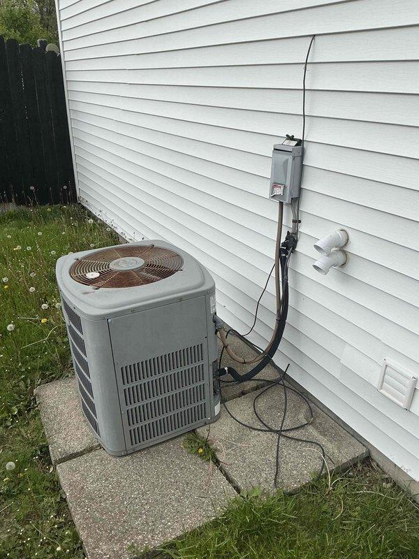 Responded to no cooling complaint for residential property with over 20-year-old air conditioning system that was non-functional. Completed full HVAC system assessment revealing existing Payne furnace in serviceable condition with Electro-air air handler present in basement utility area. Installed new outdoor condensing unit on concrete pad against exterior wall with white vinyl siding, positioned on level pavers in lawn area. Mounted electrical disconnect box on exterior siding with proper conduit routing to new condenser. Installed refrigerant line set with white PVC line covers penetrating exterior wall, connecting outdoor condenser to indoor air handler. Verified all electrical connections, refrigerant lines, condensate drainage via existing white PVC piping, and system integration with existing ductwork. System tested and confirmed operational, restoring cooling capacity to entire house.