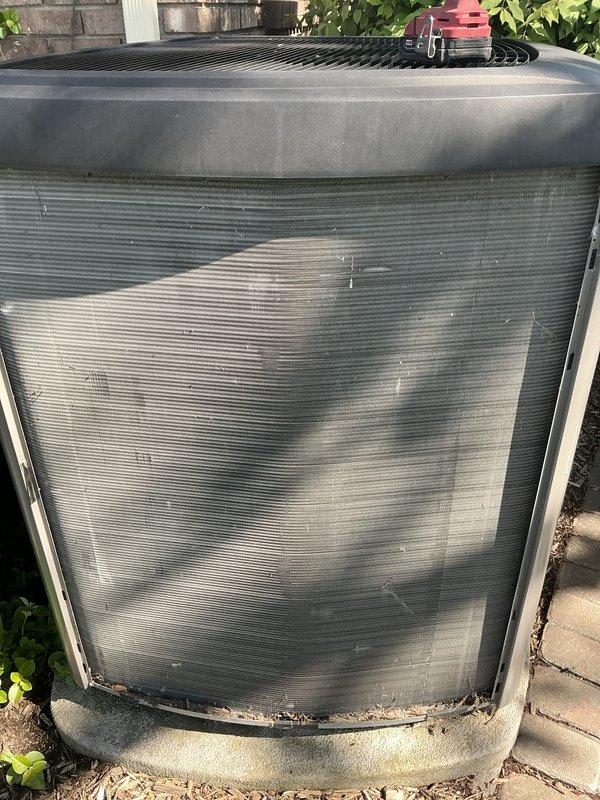 Completed comprehensive annual air conditioning maintenance and tune-up on outdoor condensing unit. Performed visual inspection of cylindrical condenser unit, noting significant environmental soiling, mineral deposits, and dirt accumulation on exterior panels requiring attention. Assessed unit placement on concrete pad adjacent to building with vegetation growth around base. Documented current system condition with photographic evidence showing exterior staining patterns and general wear. Coordinated future furnace maintenance scheduling for September as requested, establishing preventive maintenance timeline for complete HVAC system coverage throughout the year.