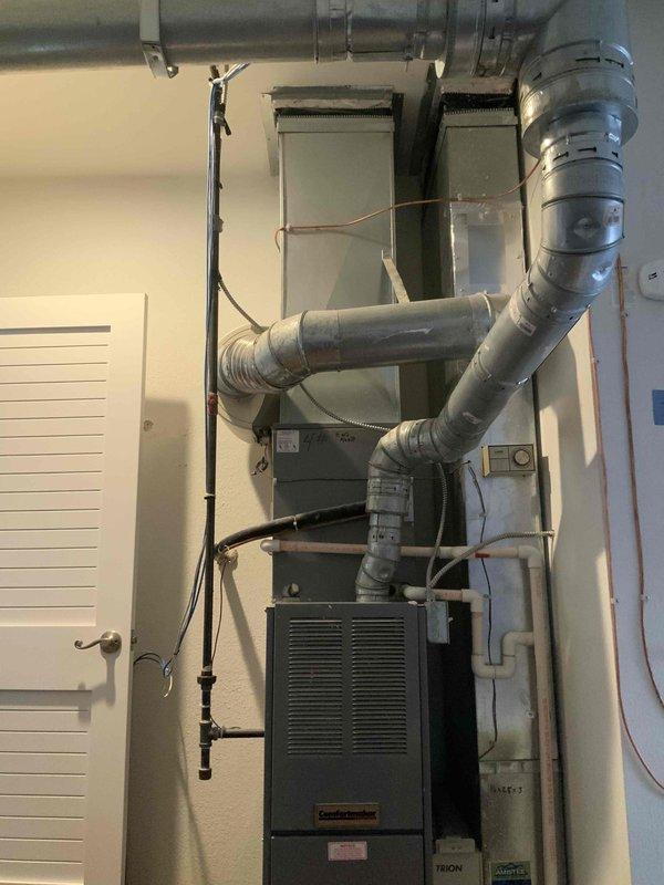 Conducted comprehensive evaluation of existing HVAC system for full replacement estimate, including air conditioning unit of unknown age and furnace approximately 23 years old. Documented current system configuration featuring vertical air handler assembly with flexible ductwork distribution, copper refrigerant lines, and existing furnace unit with metallic ductwork network. Assessed complete system for replacement recommendation, photographed existing installation showing plenum assembly, duct connections, electrical components, and overall mechanical room layout to provide accurate equipment sizing and installation planning for proposed new heating and cooling system.