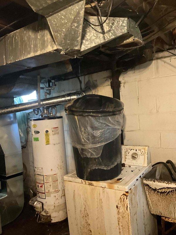 Conducted water heater replacement estimate in basement for non-operational unit of unknown age. Assessed existing white cylindrical natural gas water heater showing significant wear, discoloration, and age-related deterioration, along with associated plumbing connections and venting requirements. Documented current installation configuration including proximity to existing HVAC system, water softener equipment, and available workspace for replacement, providing homeowner with equipment options and installation recommendations.