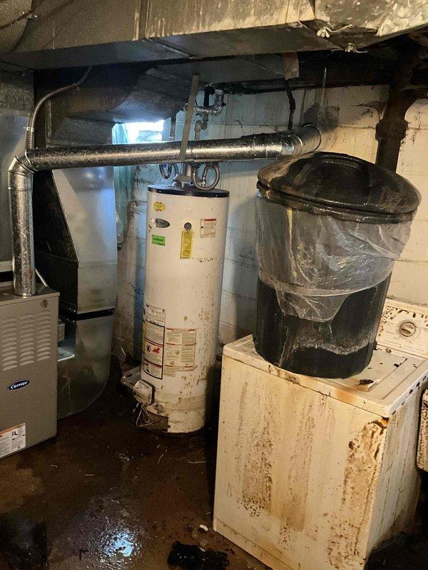 Conducted water heater replacement estimate in basement for non-operational unit of unknown age. Assessed existing white cylindrical natural gas water heater showing significant wear, discoloration, and age-related deterioration, along with associated plumbing connections and venting requirements. Documented current installation configuration including proximity to existing HVAC system, water softener equipment, and available workspace for replacement, providing homeowner with equipment options and installation recommendations.