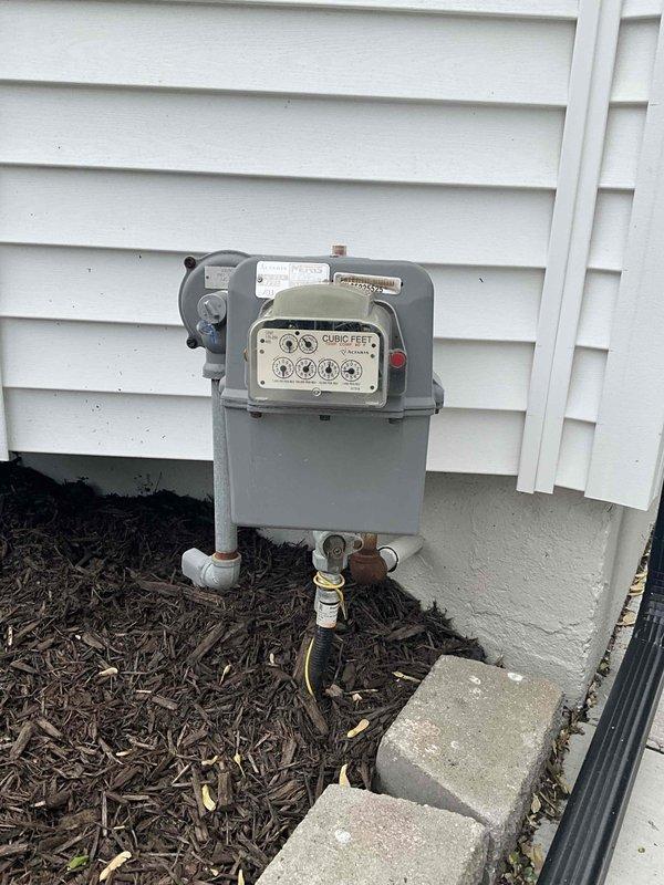Conducted comprehensive site evaluation for HVAC system replacement estimate on residential property with 10+ year-old equipment. Assessed existing outdoor condensing unit positioned on concrete pad adjacent to building exterior, noting weathered installation and age-related wear patterns. Evaluated natural gas meter installation, associated gas piping, shut-off valves, and brass fittings to determine compatibility requirements for new furnace installation. Documented basement equipment location and existing infrastructure including electrical service, refrigerant line routing, and utility connections. Photographed current system configuration, concrete pad condition, gas supply components, and exterior penetration points to support equipment sizing calculations and installation planning. Reviewed operational status of functioning system to establish baseline performance metrics and customer comfort requirements for replacement specifications.