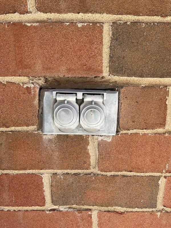 Performed comprehensive electrical inspection of 23-year-old residential property to diagnose non-functioning outlets and evaluate outdoor electrical systems. Inspected exterior weatherproof outlet receptacle mounted in brick wall, noting significant age-related deterioration, discoloration, and accumulated debris on outlet components. Removed and examined duplex receptacle, which displayed weathered housing, yellowed plastic, and compromised condition from extended outdoor exposure. Assessed electrical wiring connections and outdoor outlet box installation for proper grounding, weatherproofing, and code compliance. Evaluated electrical circuit serving air conditioning unit to verify proper operation and connection integrity.