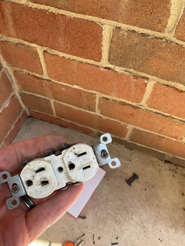 Performed comprehensive electrical inspection of 23-year-old residential property to diagnose non-functioning outlets and evaluate outdoor electrical systems. Inspected exterior weatherproof outlet receptacle mounted in brick wall, noting significant age-related deterioration, discoloration, and accumulated debris on outlet components. Removed and examined duplex receptacle, which displayed weathered housing, yellowed plastic, and compromised condition from extended outdoor exposure. Assessed electrical wiring connections and outdoor outlet box installation for proper grounding, weatherproofing, and code compliance. Evaluated electrical circuit serving air conditioning unit to verify proper operation and connection integrity.