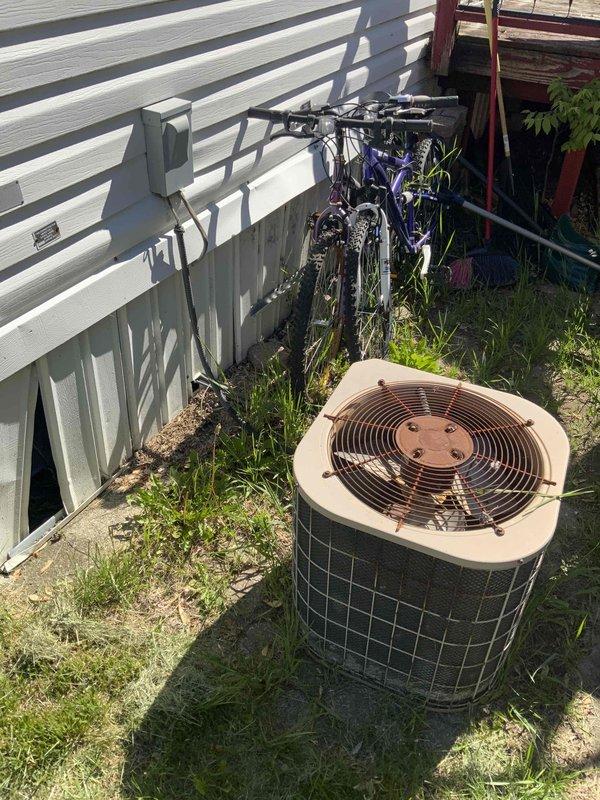 Provided estimate for replacement of non-operational outdoor air conditioning condenser unit aged 15+ years. Unit is located on exterior side yard area, positioned on ground level between main residence and secondary structure. Current equipment shows visible weathering and age-related deterioration, with unit no longer functioning and requiring full replacement to restore cooling capacity to the home.