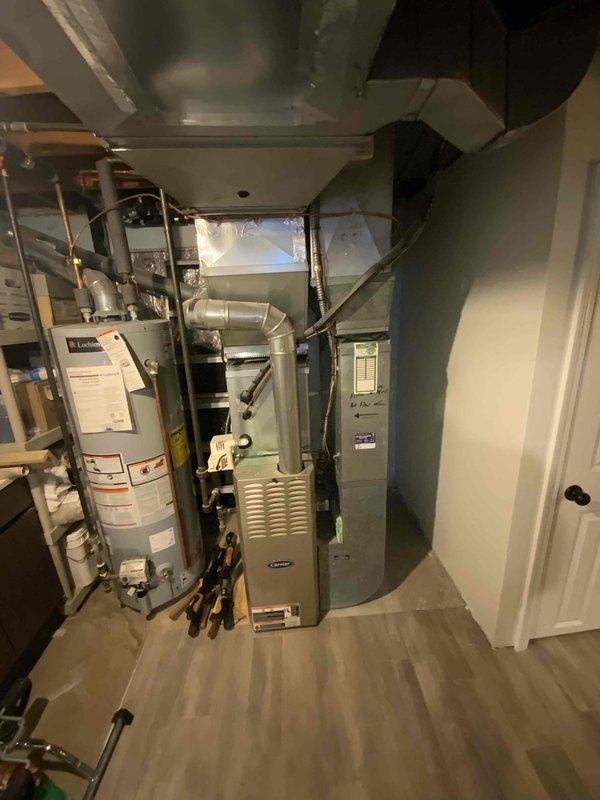 Conducted comprehensive on-site evaluation for complete HVAC system replacement estimate. Assessed existing 21-year-old air conditioning unit and furnace located in basement mechanical room. Documented current equipment configuration, including ductwork layout, electrical service panel accessibility, and existing utility connections. Photographed installation area showing furnace, water heater proximity, exposed rectangular and spiral ductwork, copper piping, and electrical infrastructure to develop accurate replacement specifications and system design recommendations.
